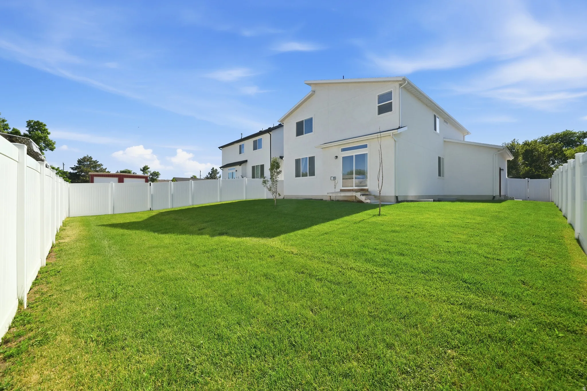 Spacious fenced backyard with vibrant green lawn, featuring a modern white two-story exterior