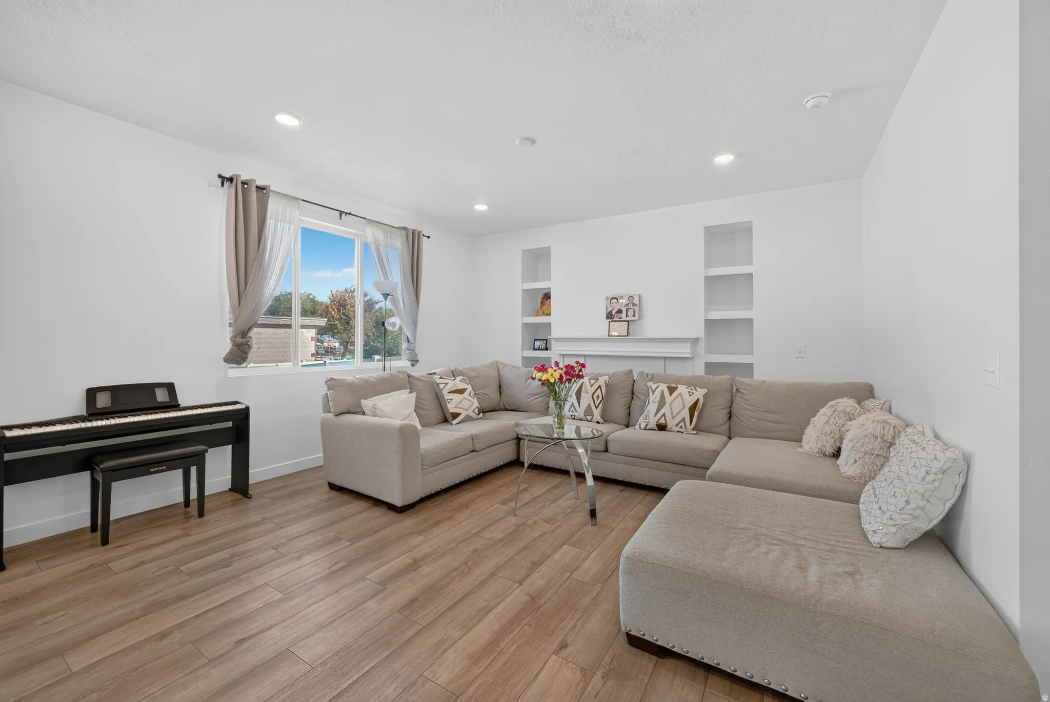 Open concept living area featuring wood-finish flooring, recessed lighting, a large window, and built-in shelving with a mantel