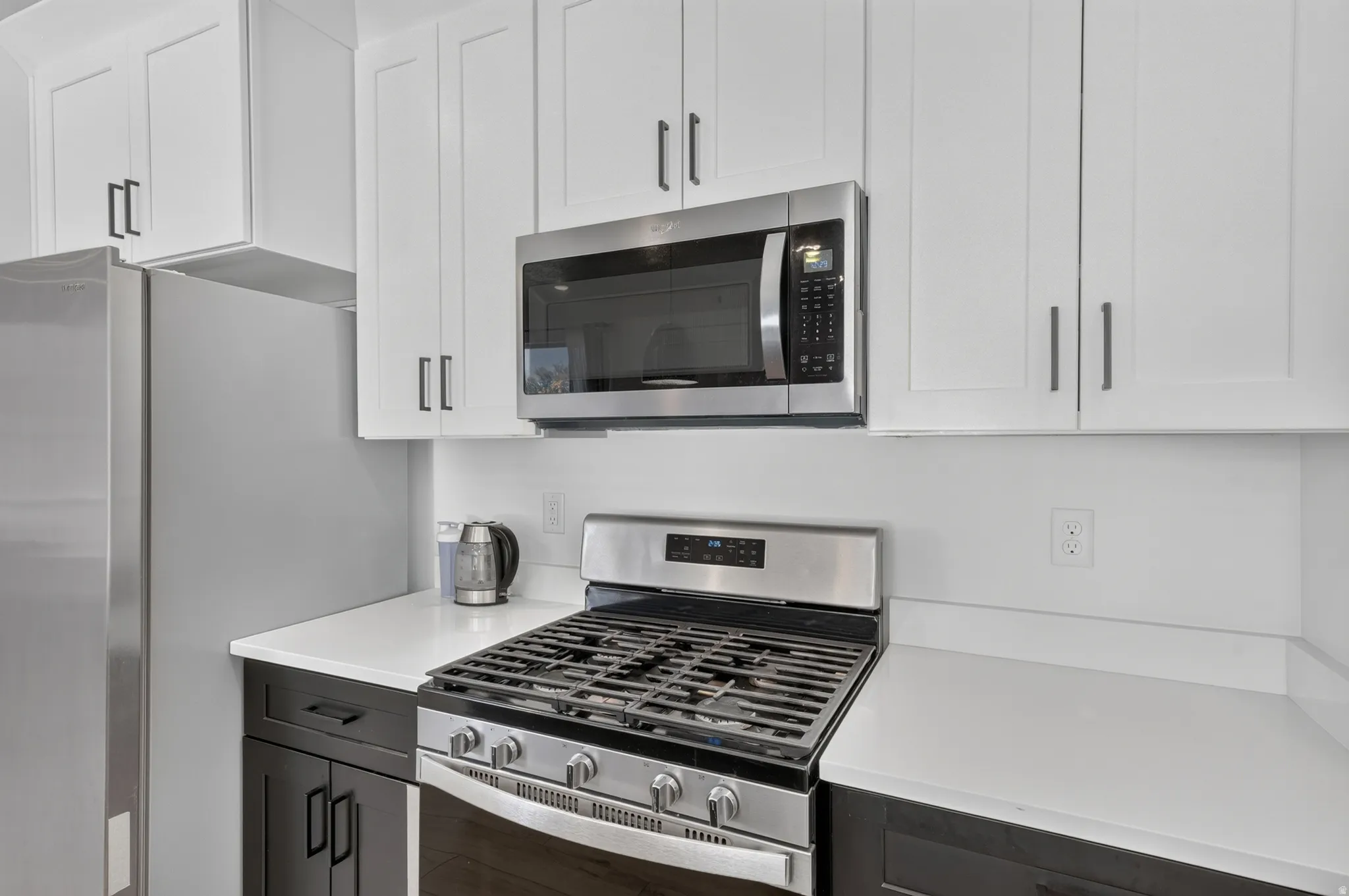 Kitchen featuring stainless steel appliances, white shaker-style upper cabinetry, dark lower cabinetry, and light-toned countertops