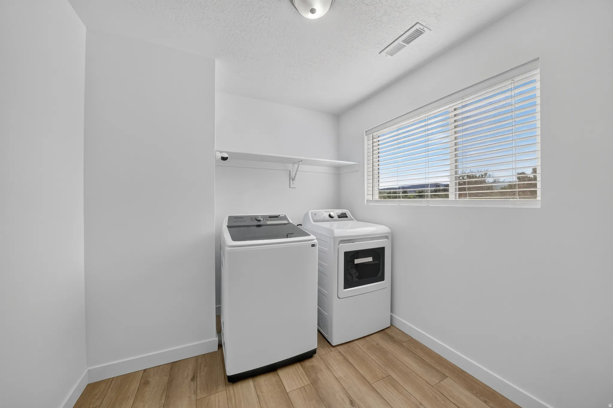 Laundry area featuring wood-finish flooring, a functional window with blinds, and a wall-mounted storage shelf