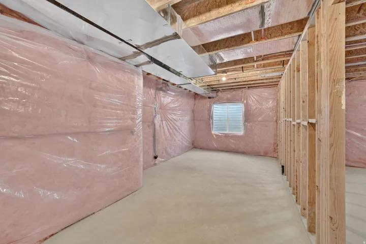Unfinished basement featuring exposed wood framing, concrete flooring, insulated perimeter walls, and an egress window