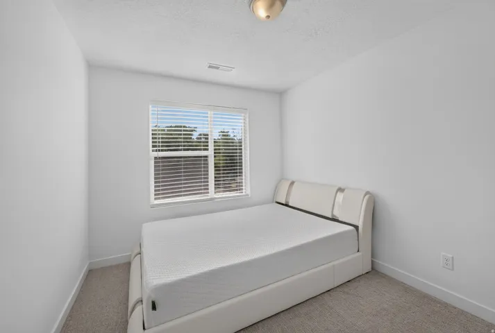 Bright room featuring a single window with horizontal blinds, neutral carpeting, and white walls