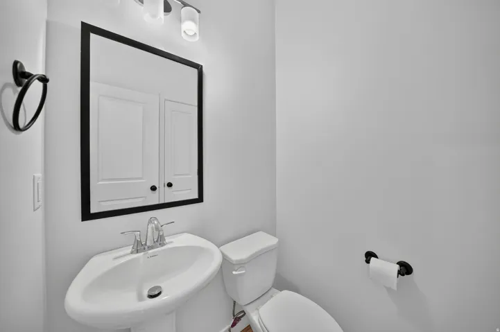 Pedestal sink with chrome faucet, black-framed mirror, and contemporary vanity lighting