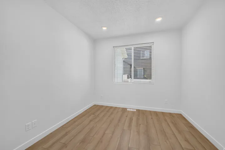Room with light wood-finish flooring, white walls, and a window with blinds