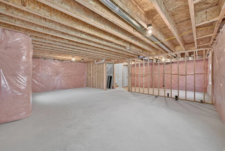 Unfinished lower level featuring exposed wood joists, concrete flooring, rough-in framing, and insulation