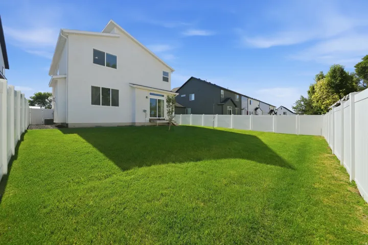 Expansive rear yard featuring a large grass lawn, full privacy fencing, and a modern white exterior with multiple windows