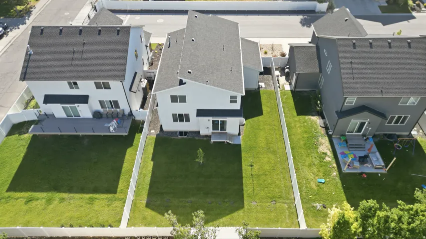 Expansive fenced backyard featuring a manicured lawn, a young tree, and a concrete patio