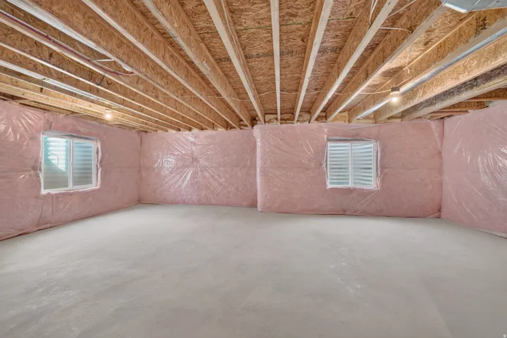 Unfinished basement featuring exposed wood joists, pink insulation, and a concrete floor