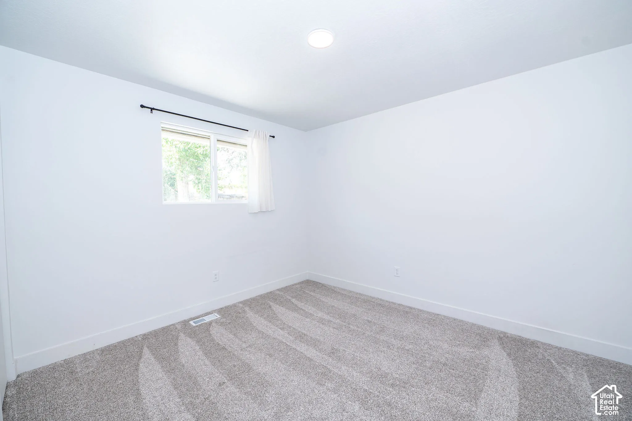 Neutral-toned carpeting paired with white walls, a single window, and a recessed ceiling light fixture