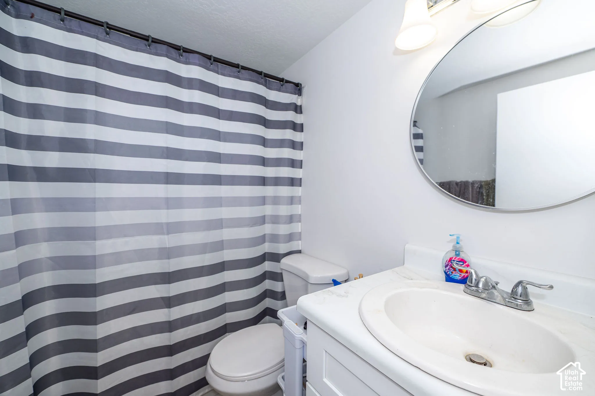 Bathroom featuring a white vanity with integrated sink, chrome faucet, and circular wall mirror