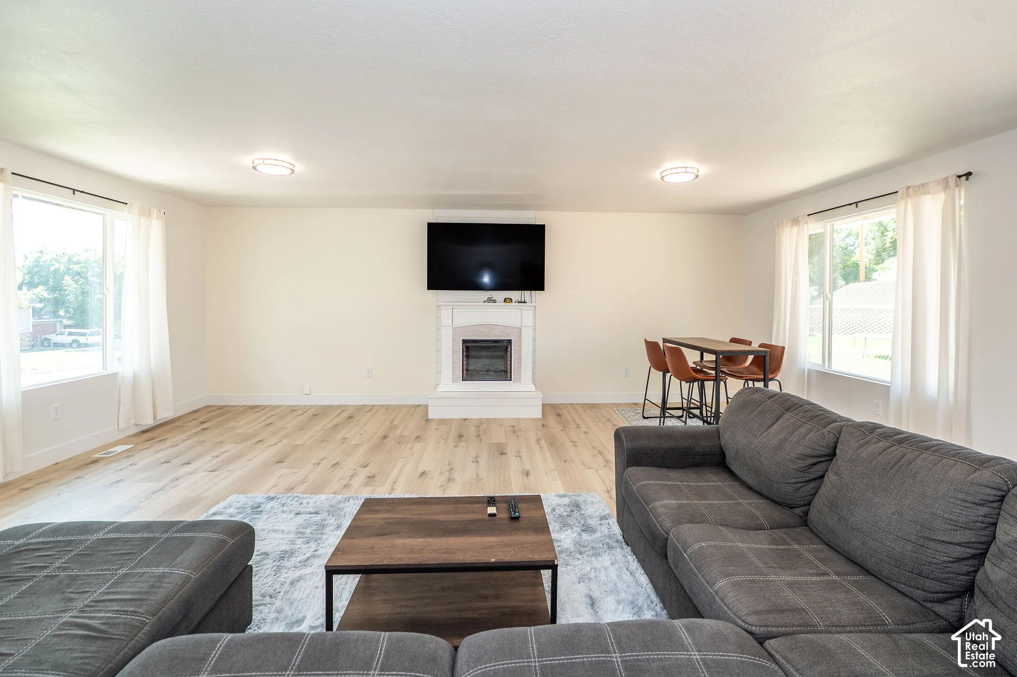 Spacious living area featuring light wood-finish flooring, white walls, and a fireplace with a white mantel