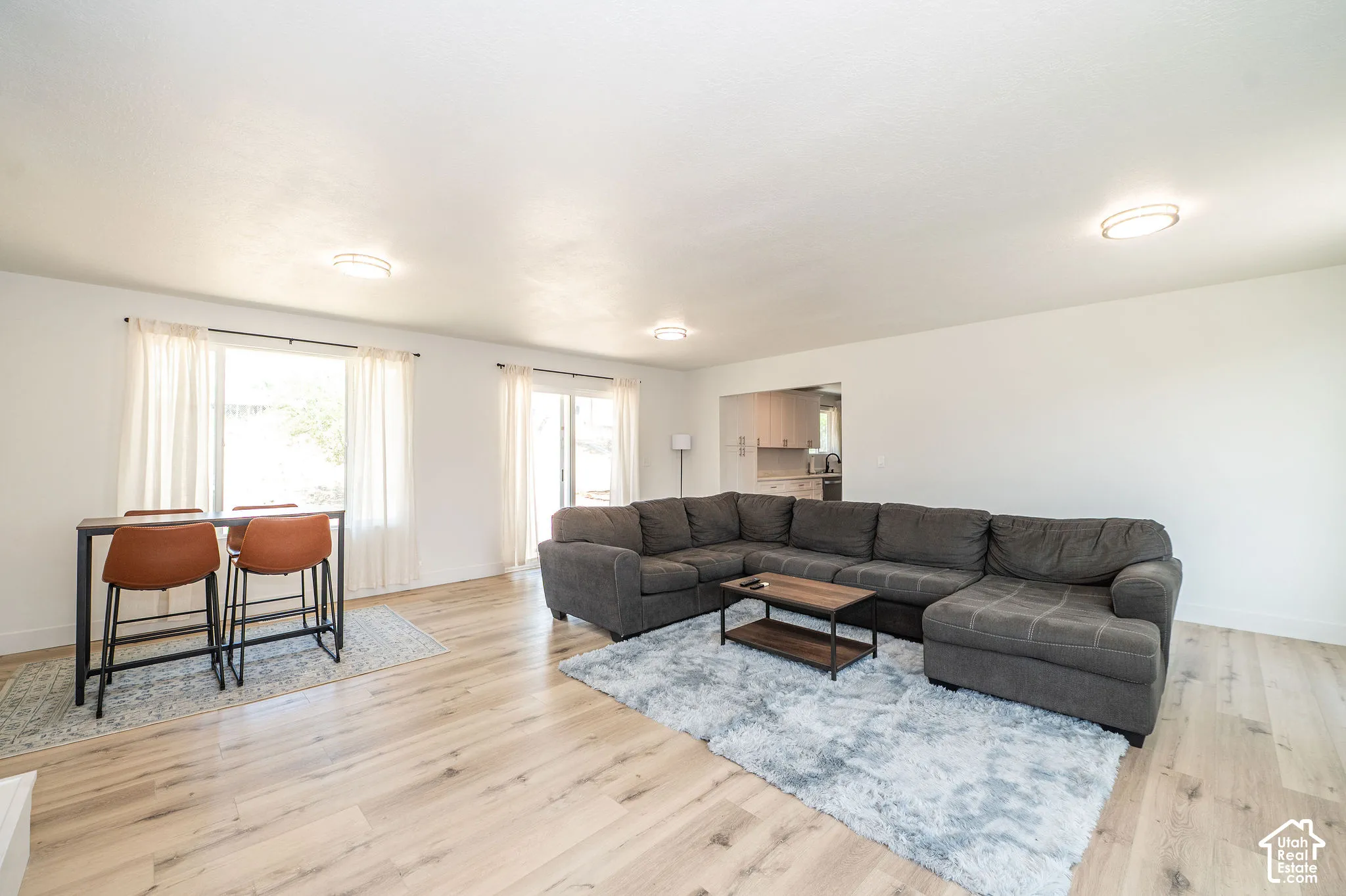 Open-concept living area featuring wood-finish flooring, white walls, flush-mount ceiling lights, and a sliding glass door