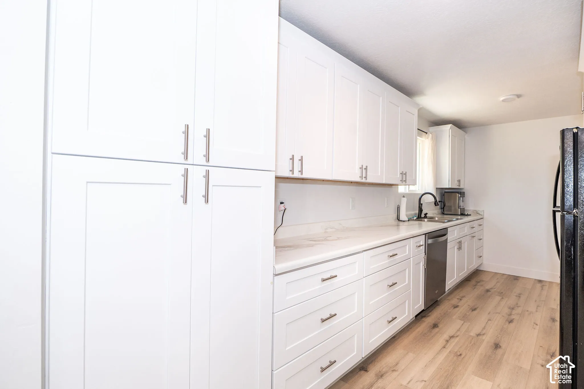 Modern kitchen featuring white shaker cabinetry, light-toned wood-finish flooring, and a stainless steel dishwasher