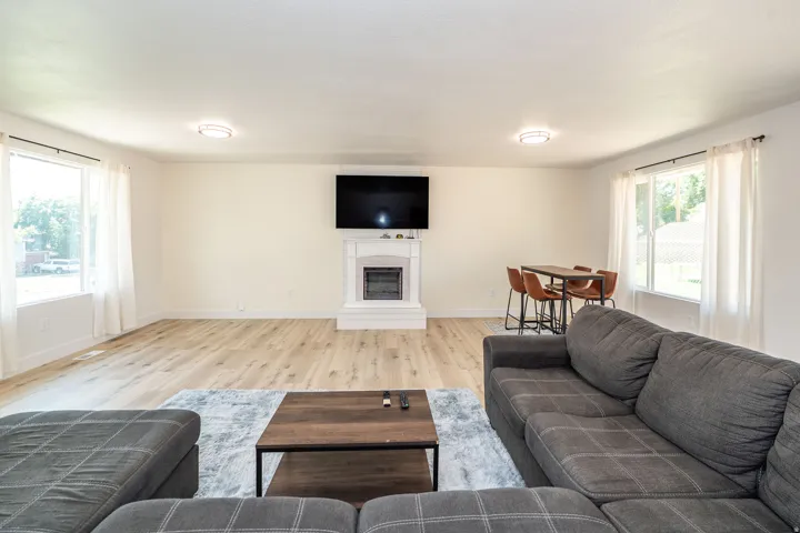 Spacious living area featuring light wood-finish flooring, white walls, and a fireplace with a white mantel