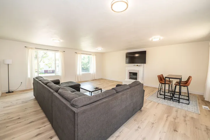 Spacious living area featuring light wood-finish flooring, multiple windows, a decorative fireplace with a mantel, and overhead flush-mount lighting fixtures