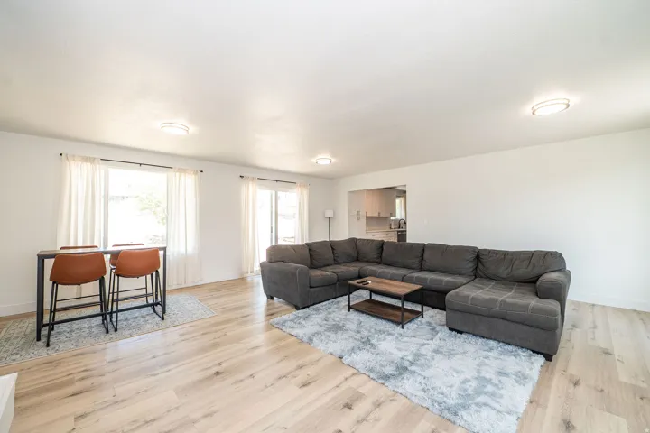 Open-concept living area featuring wood-finish flooring, white walls, flush-mount ceiling lights, and a sliding glass door