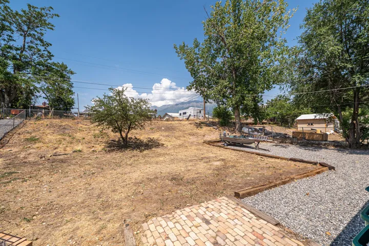 Expansive yard space featuring a gravel path, a small shed, mature trees, and a brick patio area