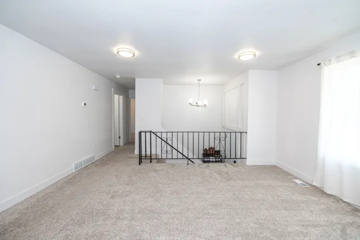 Spacious open-concept room featuring light-toned carpeting, white walls, and contemporary flush-mount lighting fixtures