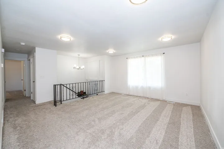 Bright room featuring light-toned carpeting, a window with sheer curtains, and a black metal railing