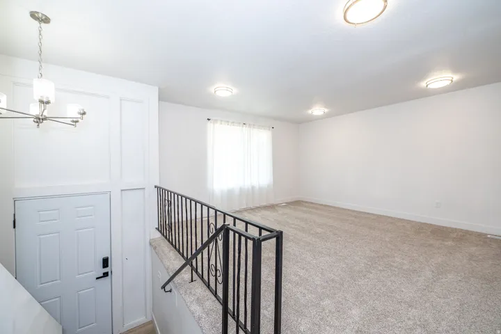 Open concept area featuring light-toned carpet flooring, multiple flush-mount ceiling lights, and a window with sheer curtains