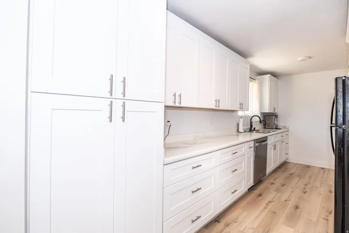 Modern kitchen featuring white shaker cabinetry, light-toned wood-finish flooring, and a stainless steel dishwasher