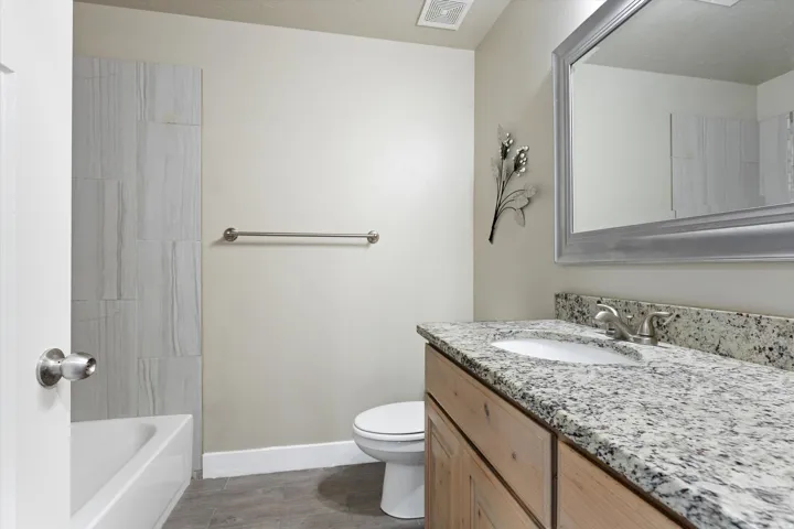 Bathroom featuring a granite-finish countertop, wood-finish vanity, undermount sink, and tiled shower surround