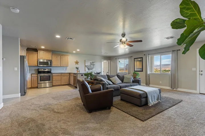 Open-concept living space featuring a carpeted floor, light oak cabinetry, stainless steel appliances, and a ceiling fan with integrated lighting