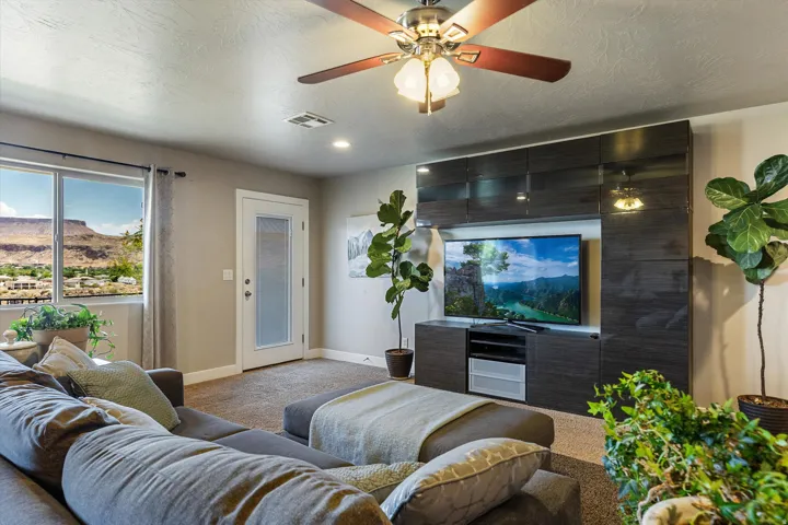 Living area featuring a floor-to-ceiling media console with dark wood-finish cabinetry, a large window with distant mountain scenery, a ceiling fan with light fixture, recessed lighting, and carpet flooring