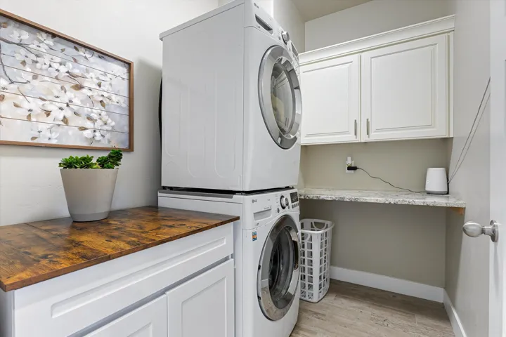 Dedicated laundry area featuring stacked appliances, overhead white cabinetry, and a light-toned countertop