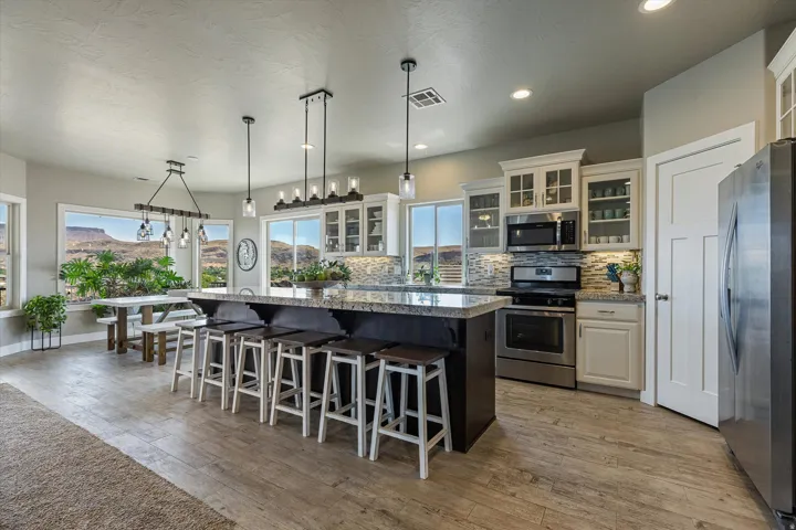 Kitchen featuring a large central island with seating, stainless steel appliances, white cabinetry with glass inserts, a tiled backsplash, and wood-finish flooring