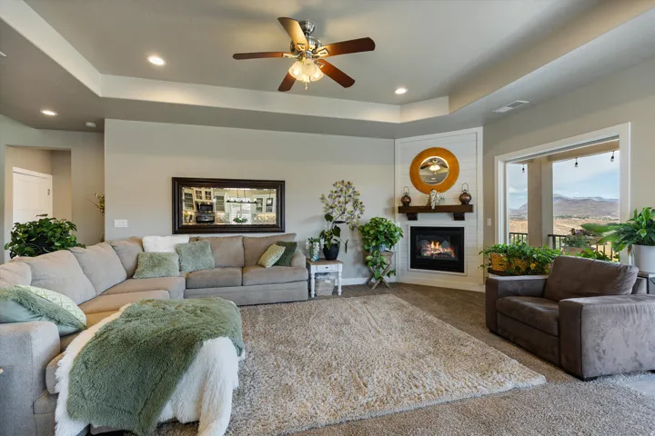 Living area featuring a corner fireplace with a wood mantle and shiplap surround, tray ceiling, recessed lighting, and an expansive outdoor opening