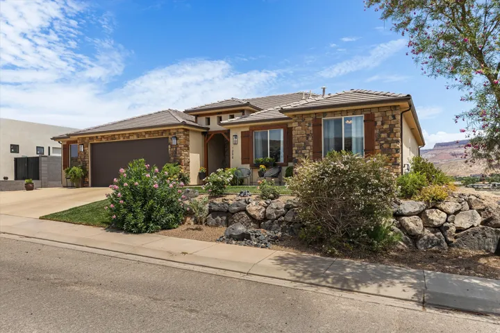 Front exterior featuring stone veneer accents, an integrated garage, a tiered rock retaining wall, front landscaping, and a mountain backdrop