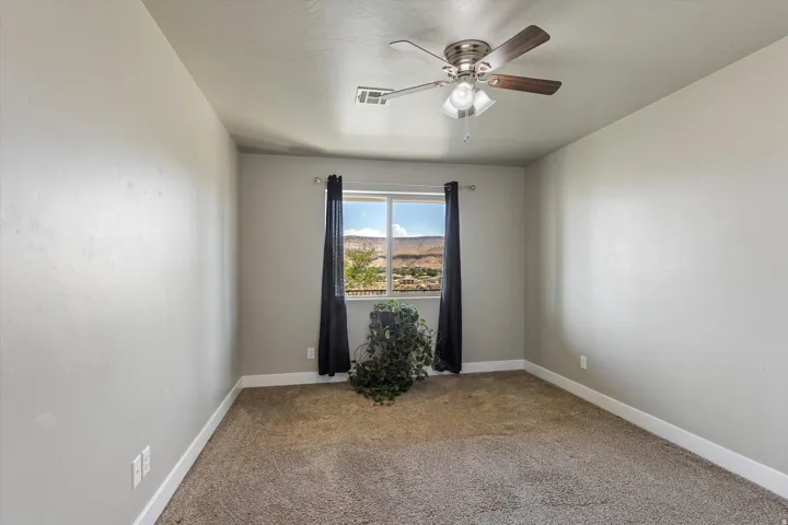 Light-filled room featuring neutral wall tones, textured carpeting, and a ceiling fan with integrated lighting