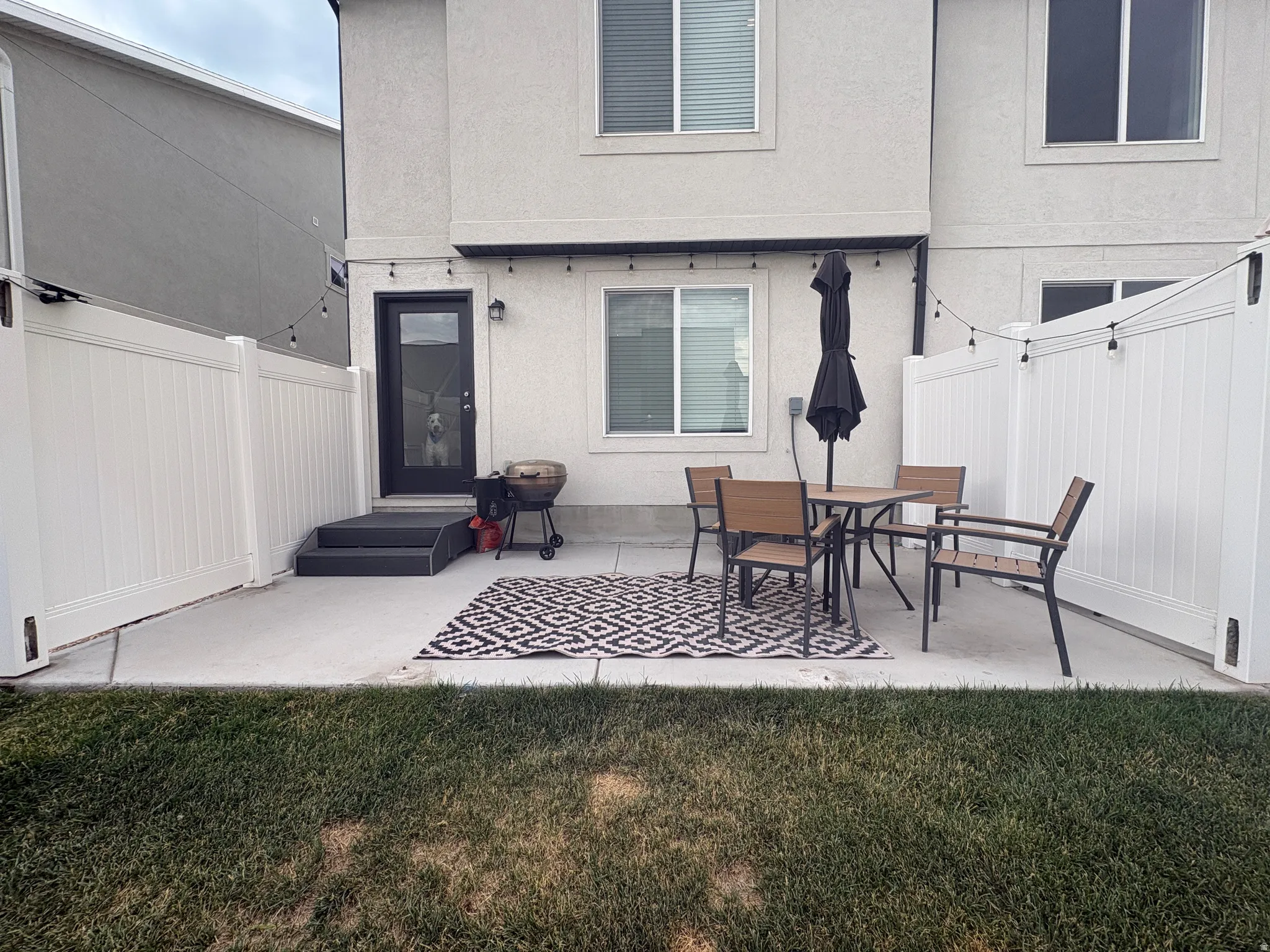 Paved patio with white privacy fencing, direct exterior entry, and string lighting