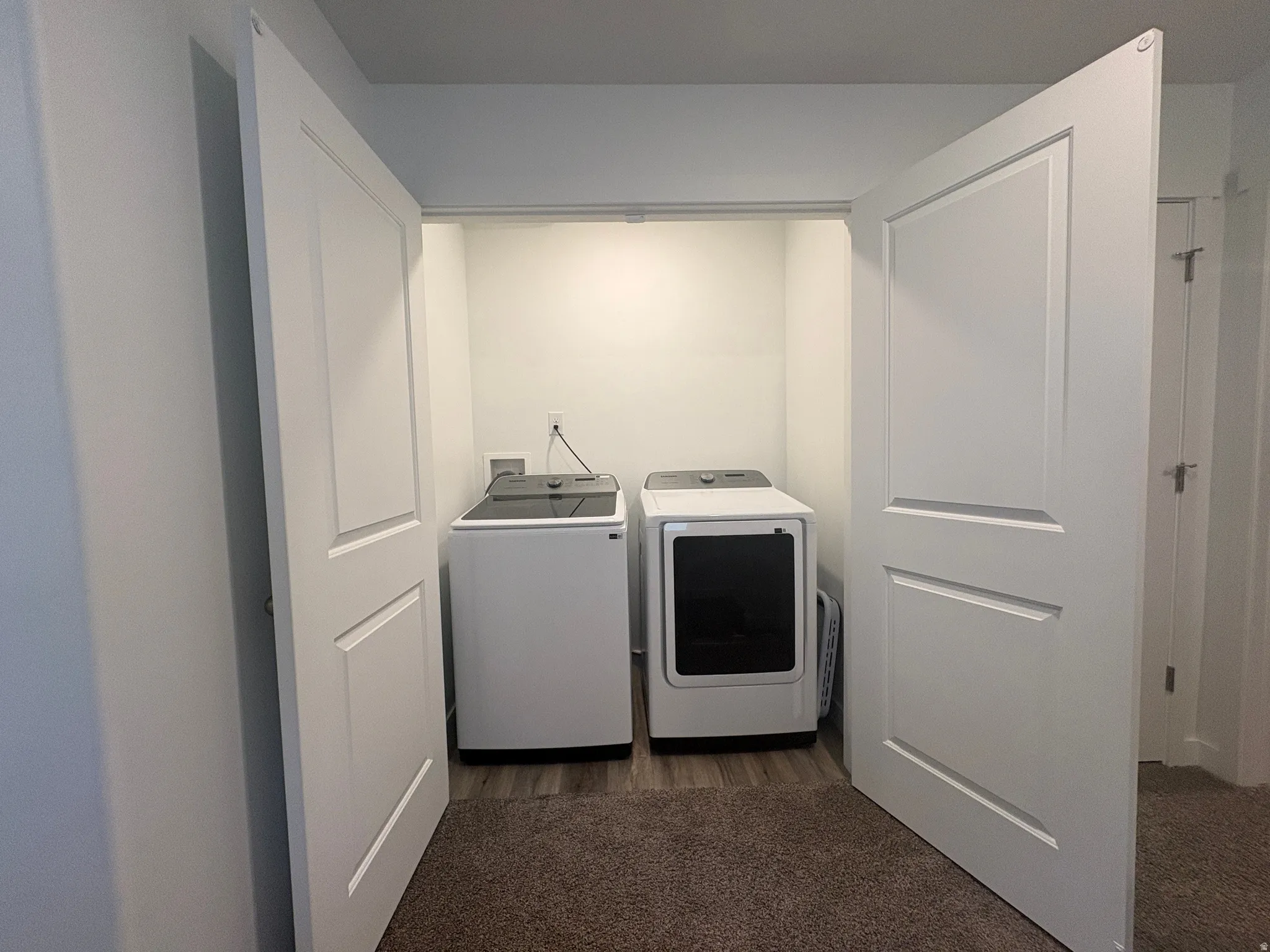 Dedicated laundry area featuring a washer and dryer, white paneled bifold doors, and wood-finish flooring