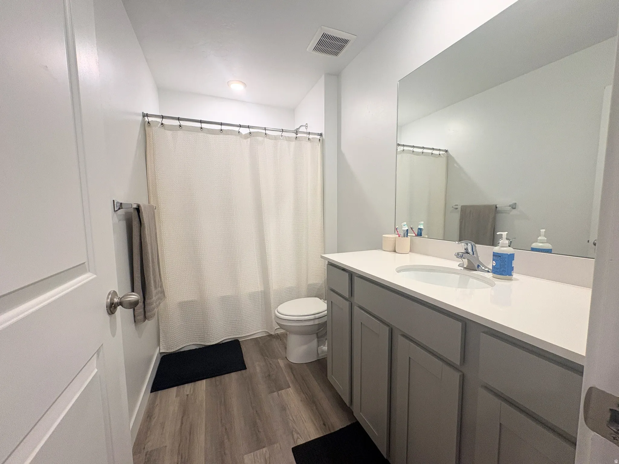 Bathroom featuring a single vanity with a white countertop and gray cabinetry, a rectangular mirror, and wood-finish flooring
