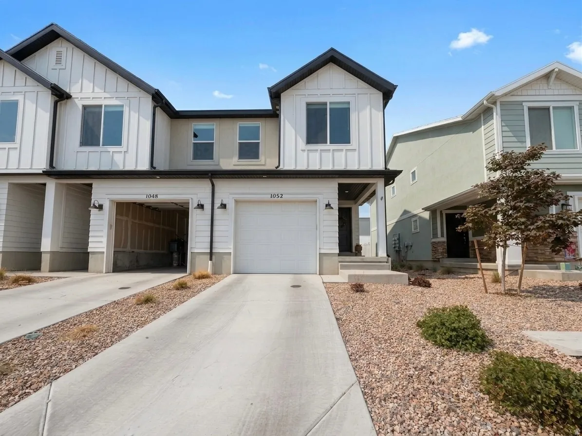 Contemporary townhome exterior featuring vertical white siding, black trim, a single-car garage, and a concrete driveway