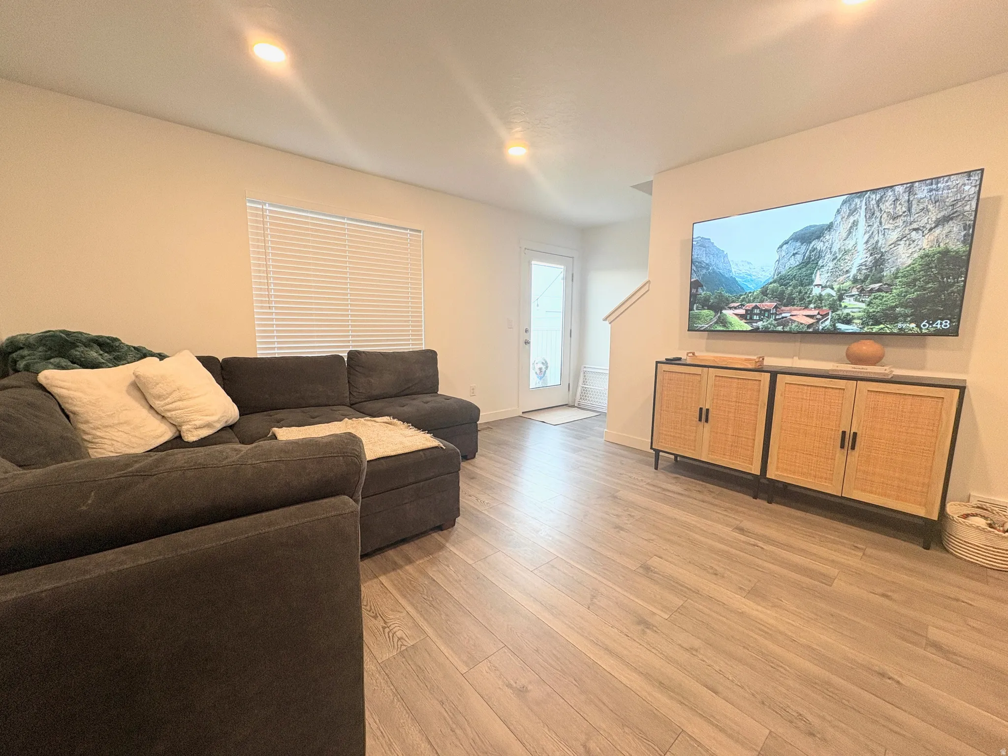 Spacious living area featuring light wood-finish flooring, recessed lighting, and a white interior door