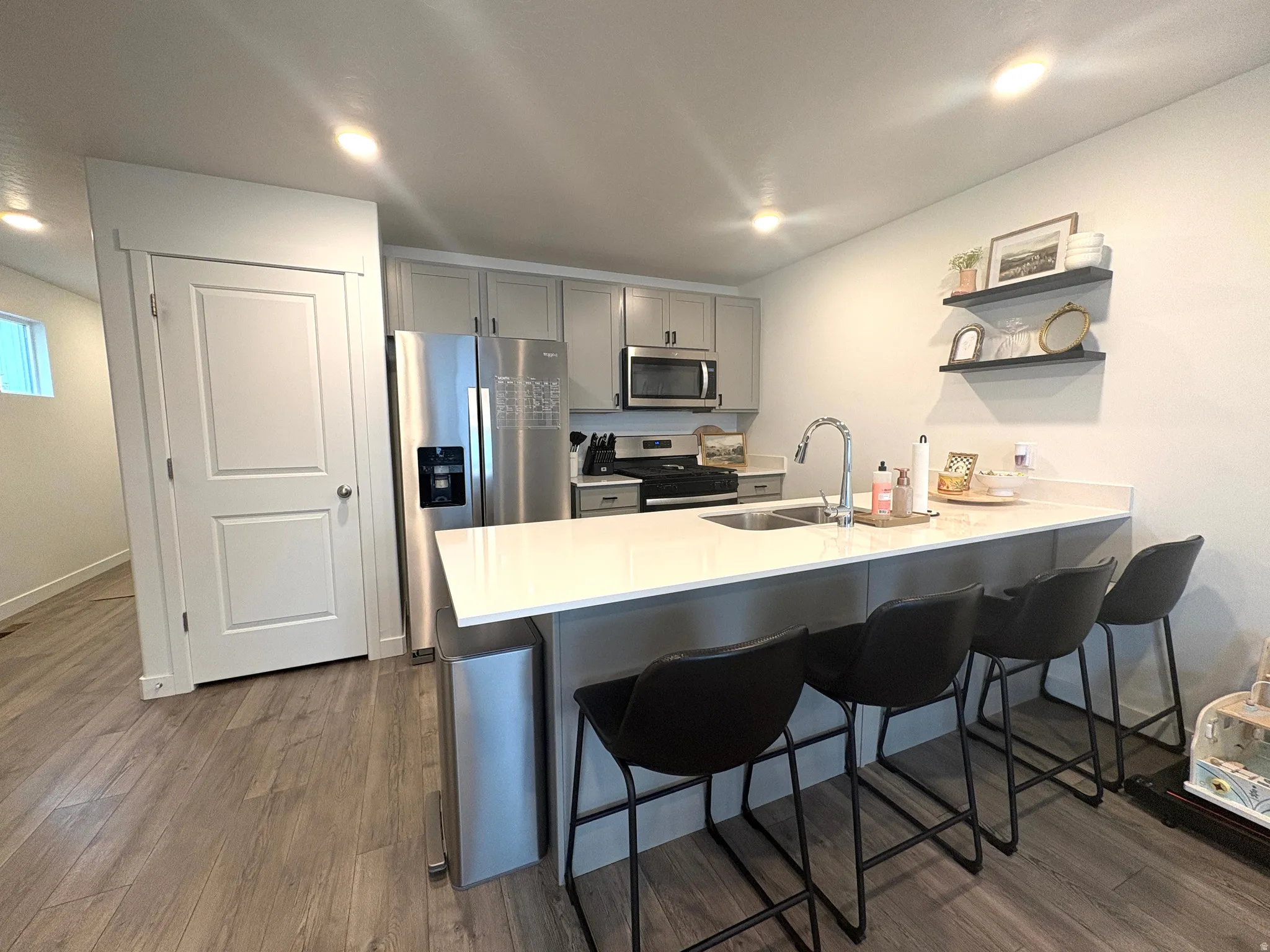 Kitchen featuring light wood-finish flooring, gray cabinetry, stainless steel appliances, and an island with a white countertop and integrated sink