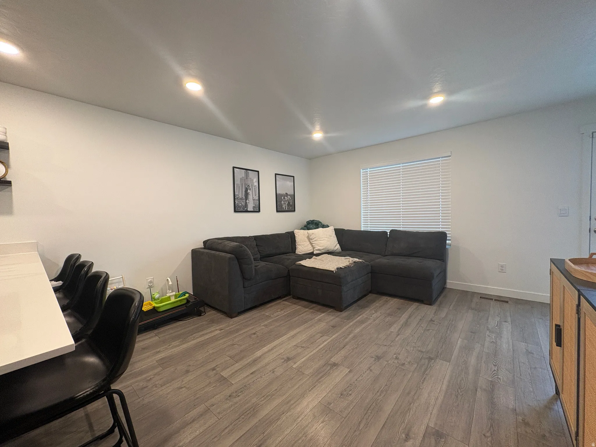 Open-concept living area featuring wood-finish flooring, recessed lighting, and a window with blinds