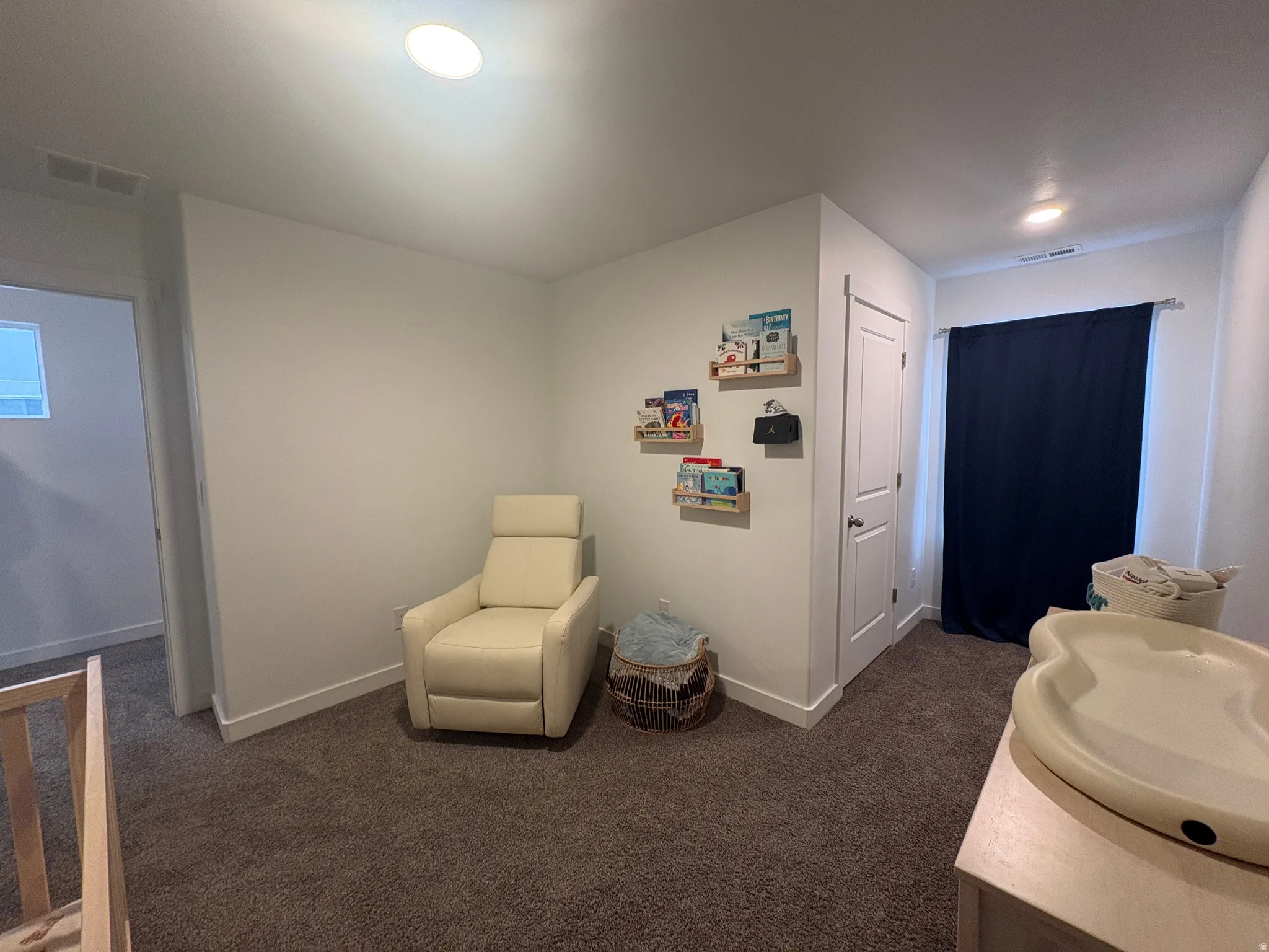 Carpeted interior space featuring recessed lighting, a white painted door, a window with dark curtains, and white baseboards