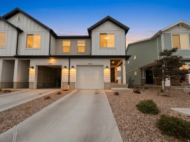 Modern townhome exterior featuring white board and batten siding with dark trim, an attached garage, concrete driveway, and covered entryway