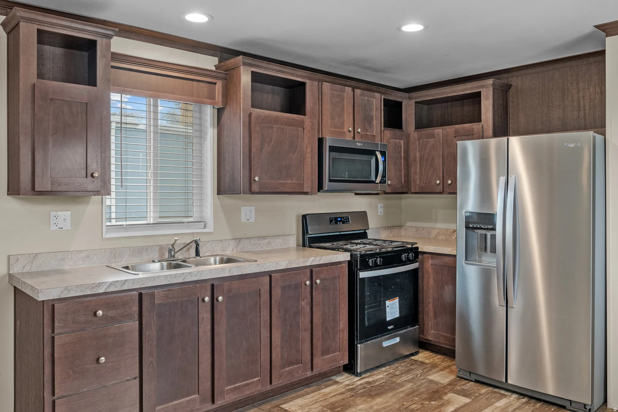 Kitchen featuring dark wood cabinetry, a double basin stainless steel sink, light-toned countertops, stainless steel appliances, and wood-finish flooring