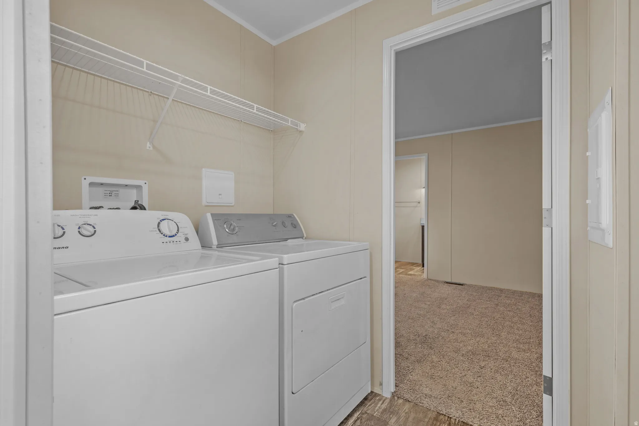 Dedicated laundry area featuring a washer and dryer, an overhead wire storage shelf, and neutral wall paneling