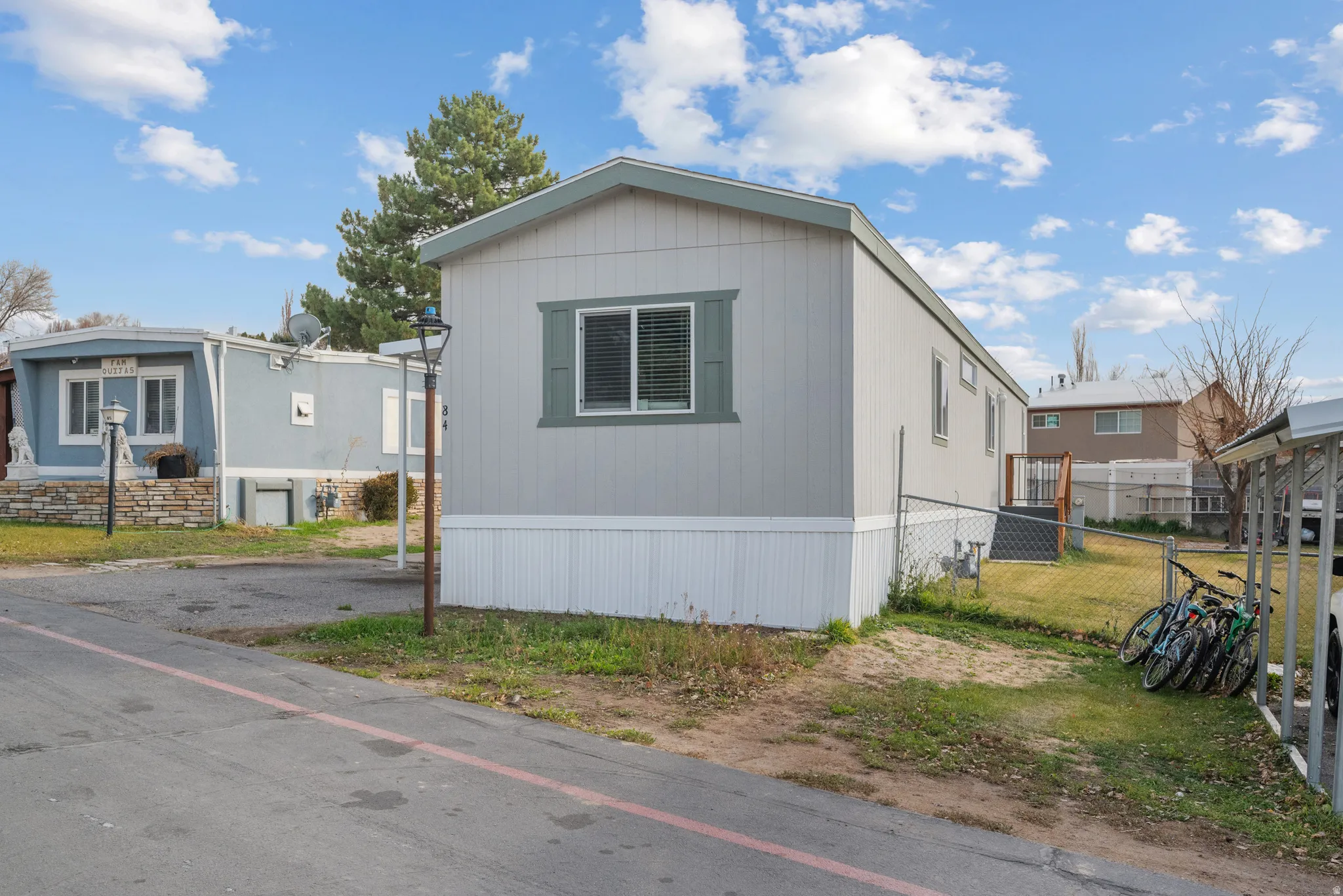 Light gray manufactured home with green trim, white window frames, and white vinyl skirting