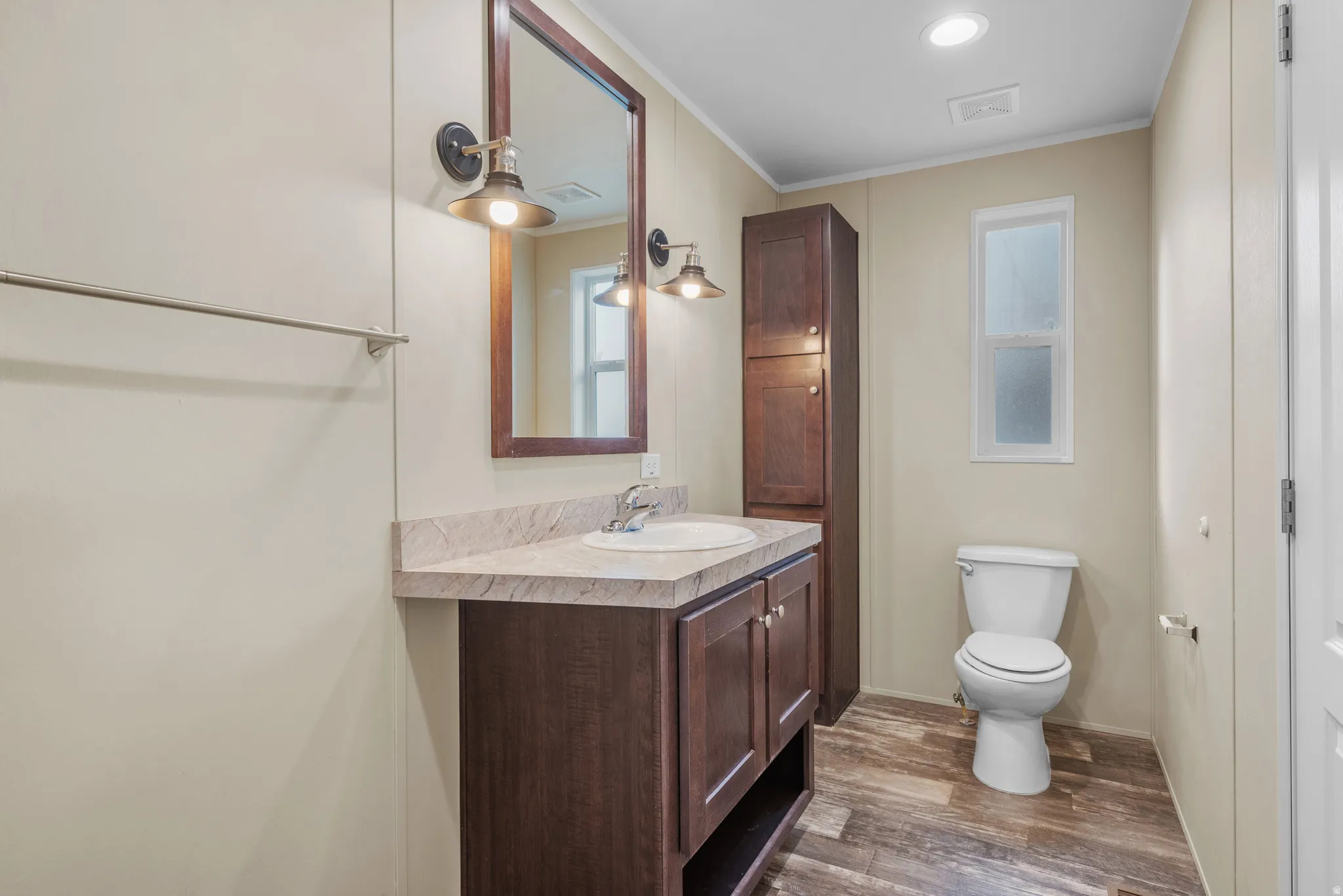 Bathroom featuring a vanity with a countertop sink, wood-finish cabinetry, and a framed mirror with industrial-style sconces