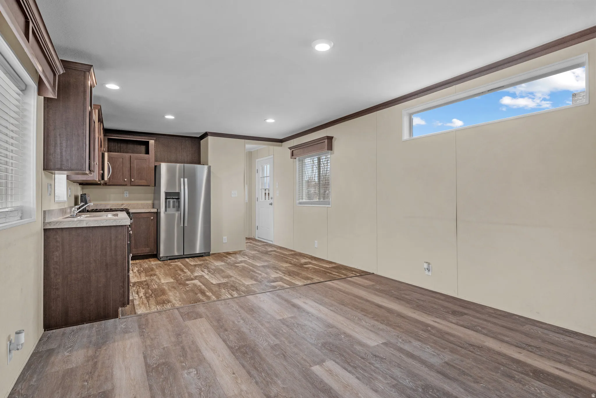 Open concept living area featuring wood-finish flooring, recessed lighting, and a kitchen with dark cabinetry and stainless steel appliances