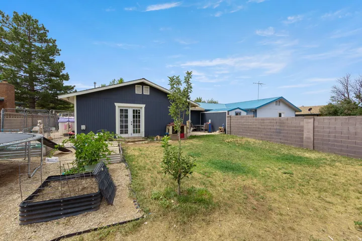 Expansive backyard featuring a partial privacy wall, a garden bed area, and a detached structure with French doors