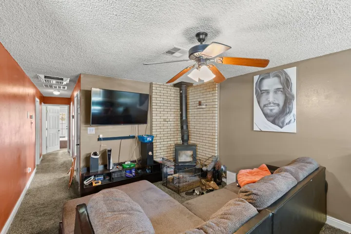 Living area with a brick-surround wood-burning stove, ceiling fan, and carpet flooring