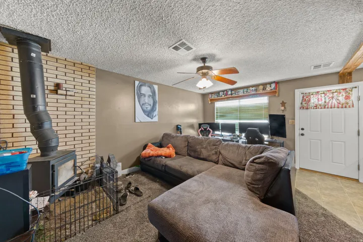 Living area featuring a brick accent wall with a wood-burning stove, a ceiling fan, and a built-in window valance
